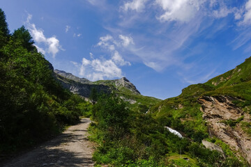 Fototapeta premium dirt road through a green mountain landscape with blue sky