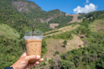 Hand holding a glass of cold espresso coffee Background blurry views tree and mountain