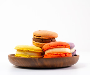 Multicolored macarons on a wooden plate on a white background.