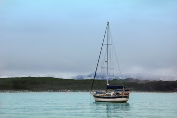 White private sailing ship on the sea in a rocky bay. Private motor ship on the background of misty mountains and forest shore