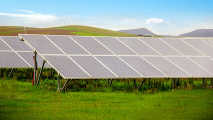 Energy storage system. Photovoltaics solar panels in power station, alternative energy from the sun in field with green grass and mountains at the horizon