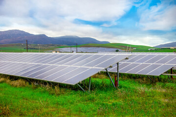 Energy storage system. Photovoltaics solar panels in power station, alternative energy from the sun in field with green grass and mountains at the horizon