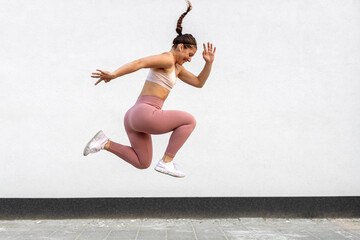 Young fitness girl in training sportswear jump high in jogging exercise outside on street.