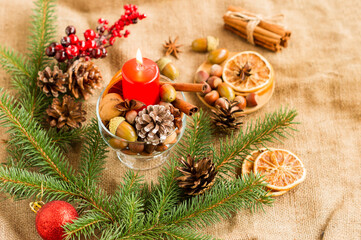 New Year's decor of red burning candle and spruce branch with cones and a ball. orange slices, cinnamon, branch with berries.