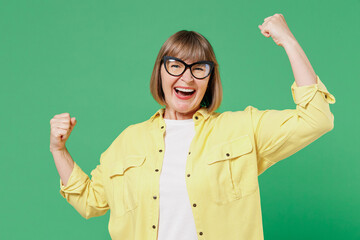 Elderly smiling happy overjoyed caucasian woman 50s in glasses yellow shirt do winnner gesture...