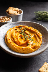 Bowl with pumpkin hummus, delicious appetizer decorated with greens and spices