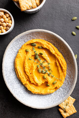 Bowl with pumpkin hummus, delicious appetizer decorated with greens and spices