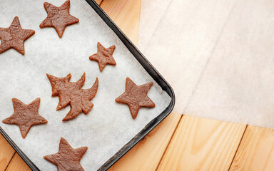 Homemade Christmas cookies on a pan. Baking paper on a wooden table. Cookies in the shape of a Christmas tree and a star.