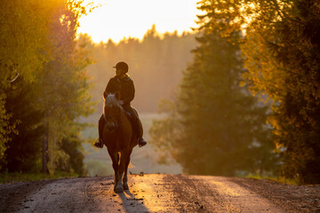 Woman horseback riding on a country road at sunset