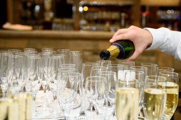 Closeup of serving champagne from the bottle in a group of champagne flutes against a colourfull background.