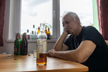 old senior male man sit next to table drink alcohol bottle at home sad alone alcoholism Signs and Symptoms rehab abuse and recovery problems