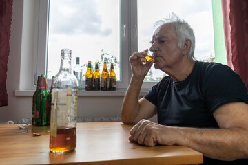 old senior male man sit next to table drink alcohol bottle at home sad alone alcoholism Signs and...