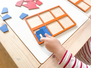The child collects puzzles. Educational wooden toy for learning. Montessori materials. Fine motor skills, hand-eye coordination. Children's leisure, nursery.The concept of early development. squares. 