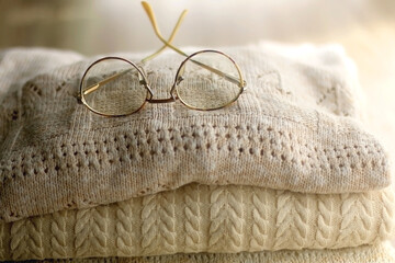 Pile of beige sweaters and retro eyeglasses. Selective focus.