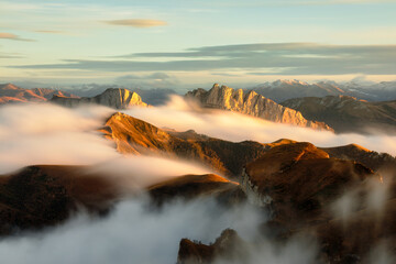 Mountains in fog at sunset in autumn. Landscape with alpine mountain valley, low clouds, forest, blue sky. Aerial view