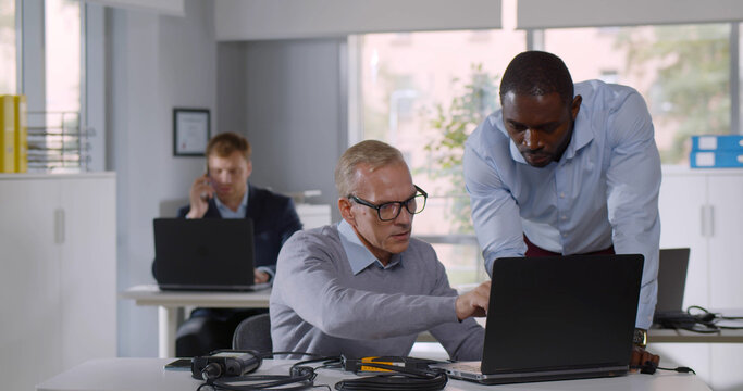 Mixed-race it-technician fix laptop for mature businessman in office