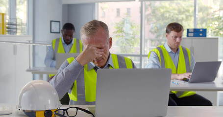 Portrait of tired industrial architect working on laptop in office