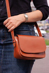 Close-up of a girl in casual clothes with a brown leather bag. Outdoors.