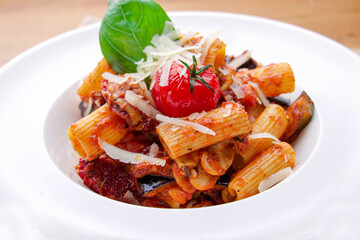 Penne pasta with tomato sauce, parmesan cheese and basil on dark background.