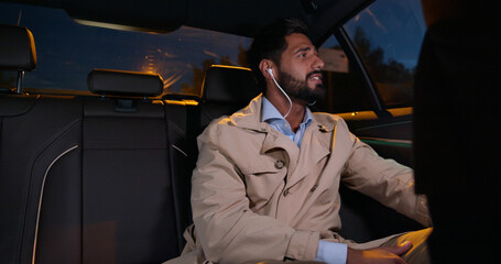 Young businessman listening music through earphones traveling on backseat in car