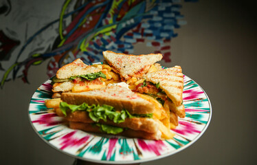 Classic club sandwich on a colored plate. The sandwich filling includes ham, cheese, lettuce, tomato slices. Light background. Close-up.
