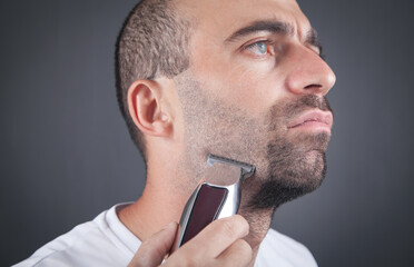 Caucasian man shaving with electric trimmer.