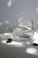 Glass of water with green capsules. Food supplements for immunity. Morning routine 