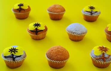Rows of muffins decorated with powdered sugar and yellow flower shaped icing on a yellow background