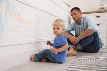 Upset father watching his little son drawing on wall at home