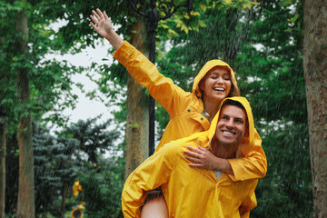 Lovely couple with raincoats having fun under rain in park