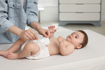 Mother changing baby's diaper on bed at home, closeup