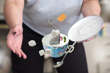 A female in gray t-shirt dropping teacup with teabag sugar cubes and spoon, selective focus