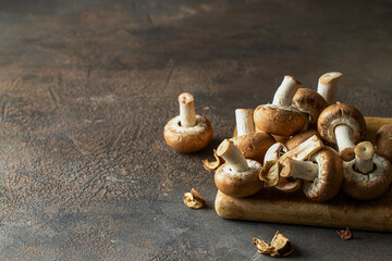 Fresh portobello mushrooms on wooden board with autumn leaves  in the dark background. © vasanty