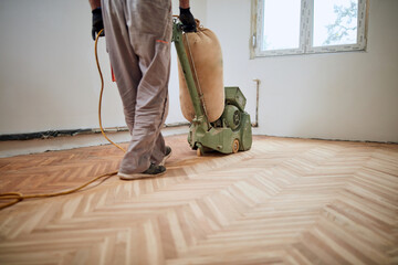 Repairman restoring parquet with a sanding machine. © astrosystem