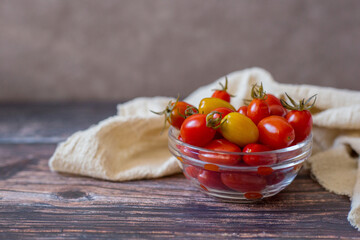 Pickled cherry tomatoes in glass bowl with beige towel on wooden background