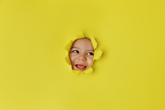 Happy baby face peeking through yellow torn paper