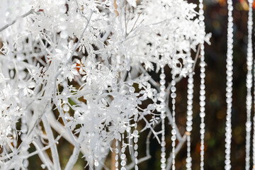 Glass, plastic, transparent beads in the form of crystals hang as decorations on the holiday close-up. White decor. Wedding ceremony on the street on the green lawn.