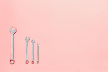 Four metal wrenches of different sizes isolated on pink background with copy space. Conceptual idea of the differences between: boss and employee, older and younger, big and small, parent and child