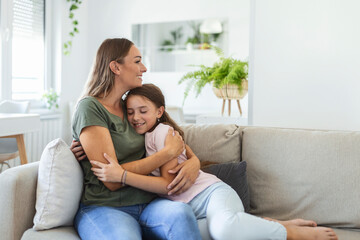 Close up of sweet pretty daughter cuddling with her young mother. Lovely mother embracing her cute daughter on the sofa at home.