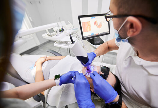 Dentist and his assistant scanning patient's teeth with modern scanning machine. Digital print of patient's teeth is on big screen. Modern high precision technologies. Concept of digital dentistry