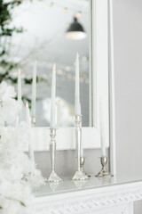 Candles in a silver candlestick. LED backlight. Candles with candlesticks on the countertop with an imitation fireplace against the wall.