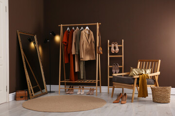 Modern dressing room interior with clothing rack, mirror and comfortable armchair