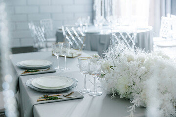 Round table with transparent plastic chairs. Flower arrangement in the center of the table. The interior of the restaurant for a wedding dinner. A round banquet table is set. The concept of catering. 