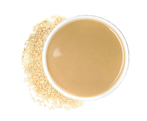 Tasty sesame paste in bowl and seeds on white background, top view