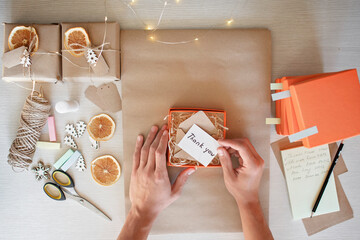 Young millennial worker packing Christmas gift boxes for clients, family small business. New Year celebration, distant work and home office, indoor lifestyle, top view