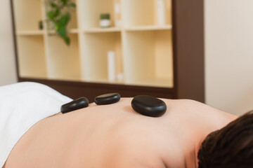 Cropped view of hot stones on back of man in spa center