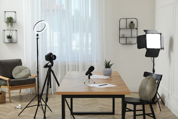 Camera and lighting equipment on tripods near table in room. Blogger workplace