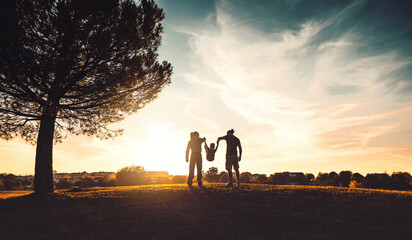 Silhouette of happy family walking in the meadow at sunset  - Mother, father and child son having...