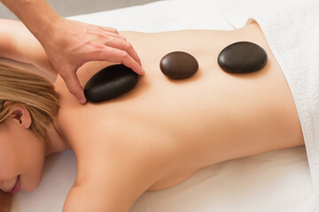 Top view of masseur putting spa stone on back of young woman on massage table