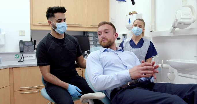 Caucasian male patient sitting in doctors chair while male and female nurse examine teeth 
